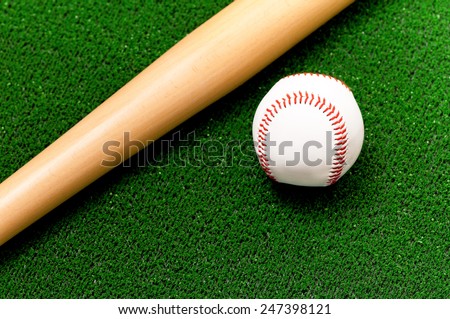 Close-up of baseball ball and bat on artificial green grass