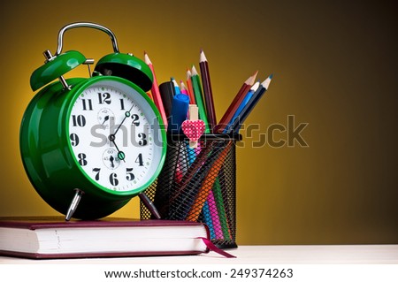 Big green alarm clock with notepad, black holder and pencils on dark yellow background