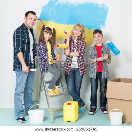 Happy family makes repairs at home. Smiling family painting big Ukrainian flag on wall at home