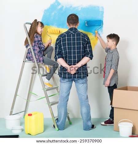 Happy family makes repairs at home. Smiling children painting big Ukrainian flag on wall at home