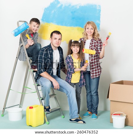 Happy family makes repairs at home. Smiling family painting big Ukrainian flag on wall at home