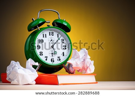 Big green alarm clock with red book and crushed paper on dark yellow background