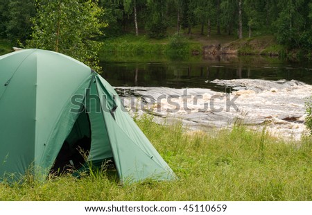 Tent set up for camping in wood by a river