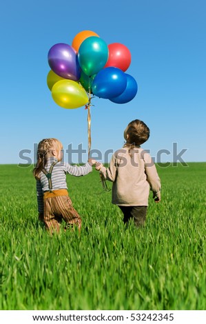Happy sister and brother with balloons walking on the spring field