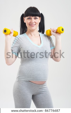 Pregnant woman in a fitness workout using hand weights on grey background