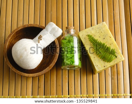 Bar of natural handmade soap with fern ,salt in glass ,massage ball in bowl on wooden mat