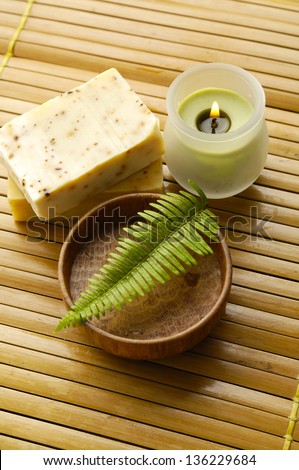 Bar of natural handmade soap with fern in bowl ,candle on wooden mat