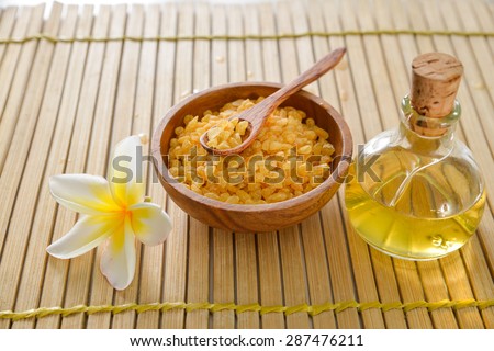 frangipani and massage oil with salt in bowl on wooden mat