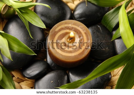 Burning candles and green plant with massage stones on woven mat