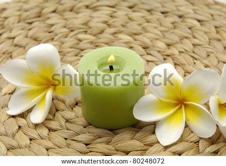 frangipani flowers with burning green candles on woven wicker mat