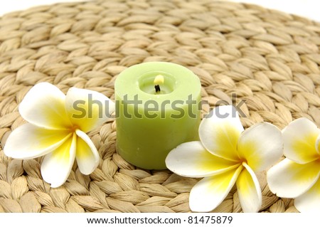green burning candles with frangipani flowers on woven wicker mat