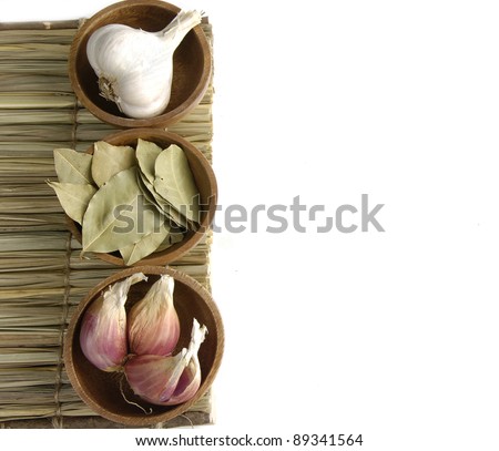 Border of dry bay leaf with garlic and garlic heads in a wooden bowl
