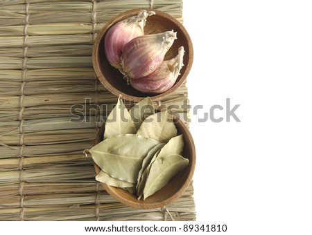 wooden bow of garlic with dry bay leaf on straw background