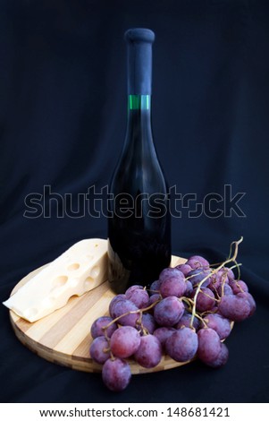 bottle of wine, grapes and cheese on the board on a black background