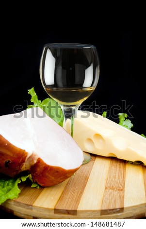 wineglass of white wine cheese and ham on a black background