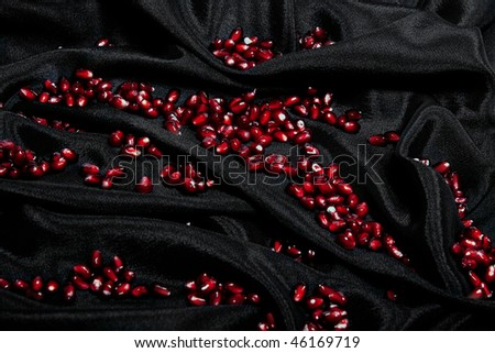 Ripe corns of pomegranate on black silk fabric .