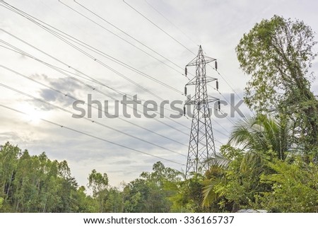 High-voltage power transmission tower. electricity transmission against blue sky and trees