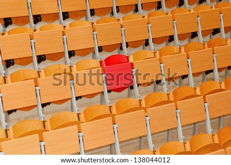 Empty classroom with wood chairs and one red chair.