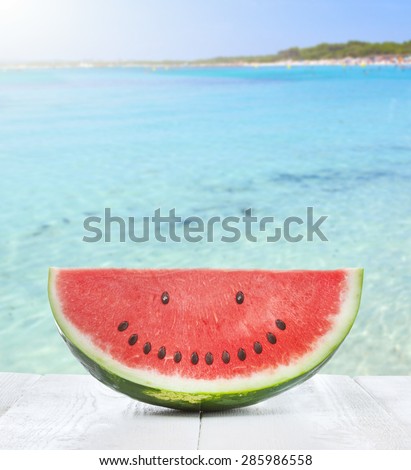 Slice of watermelon with seeds that make a smiling face on the beach