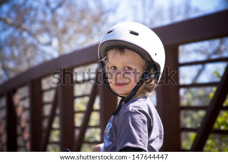 Little boy with bike helmet looking at camera with a cute half smile. Bridge in background.