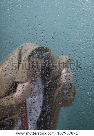 Businessman in rain behind wet window