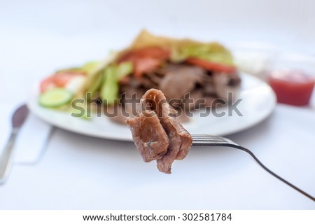 Donner meat kebab in a fork in focus and salald, pita bread not in focus on a white background