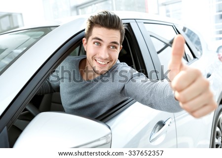 Dream came true. Cheerful casual guy smiling happily showing thumbs up sitting in a big white car