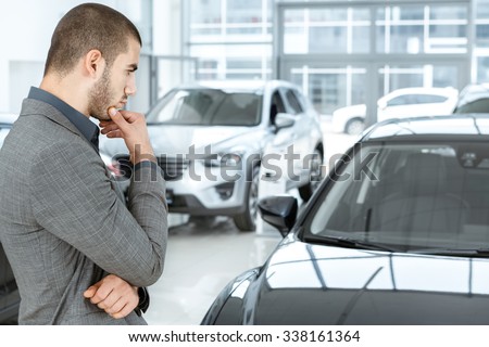 Making his choice. Horizontal portrait of a young man in a suit looking at the car and thinking if he should buy it
