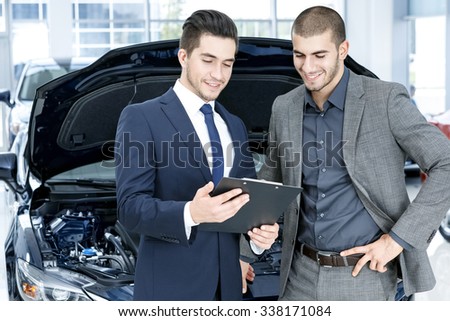 This is what he needs. Smiling car salon manager talking to a happy client in a suit