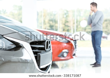 Choosing carefully. Selective focus on a car, man thinking which car to buy on the background