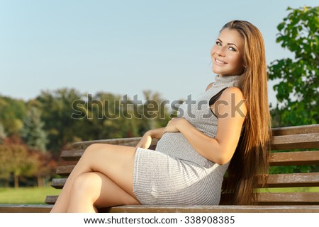 Smile for the camera. Cheerful pregnant woman smiling to the camera enjoying last summer days in the park