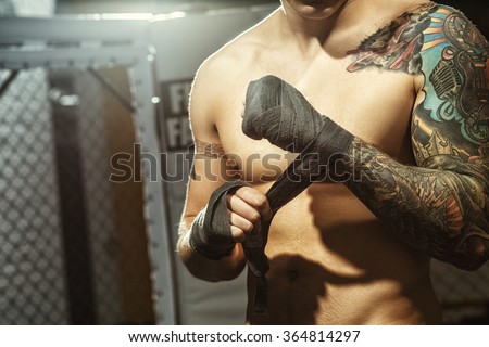 Fighting preparation. Cropped shot of a ripped tattooed fighter wrapping his hands