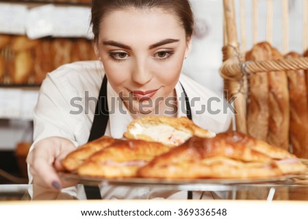 Made with love. Beautiful young female baker placing freshly baked croissants to the showcase