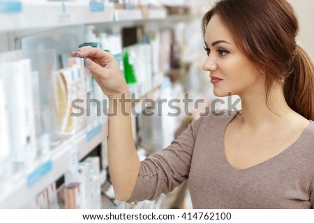 Just what I need. Horizontal portrait of a young cheerful woman customer choosing products in an aisle at the drugstore.