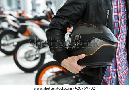 Life care. Closeup cropped shot of a male customer holding a black matte motorcycle helmet posing near a motorbike