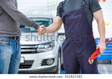 Thank you for your trust. Cropped shot of a mechanic shaking hands with the car service client repaired car on the background
