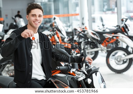 Man shopping. Portrait of a handsome cheerful man posing on his new motorbike holding out the keys smiling to the camera joyfully