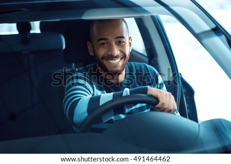 Driving gets him so excited. Shot of a handsome African man sitting in a car holding steering wheel smiling happily to the camera