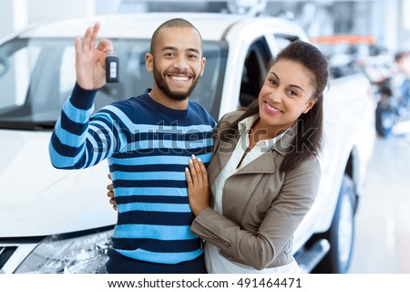 Off we go. Portrait of a happy mature couple smiling to the camera cheerfully posing near their newly bought car at the dealership handsome man holding out the car keys while embracing his wife
