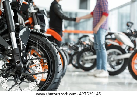 Thanks for help. Selective focus on a motorcycle wheel male customer shaking hands with motorbike salon manager on the background