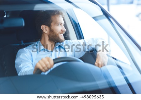 Happy owner. Handsome bearded mature man sitting relaxed in his newly bought car looking out the window smiling joyfully