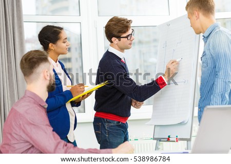 Creating ideas. Young handsome project manager leading the meeting of a creative team in the office drawing on the flipchart brainstorming with his colleagues teamwork concept