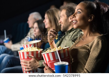 Night of joy. Beautiful African woman holding her popcorn bucket smiling joyfully while watching a movie at the cinema with her friends copyspace
