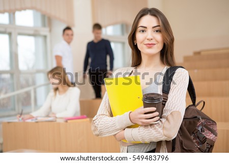 Education first. Beautiful female college student holding her books smiling happily standing in an auditorium people education learning high school program smart teenager concept copyspace