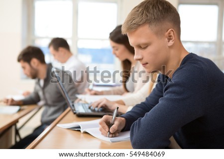 Serious studying. Young handsome male student writing during the university lecture auditorium classroom studying learning education knowledge industry degree session exam college campus concept