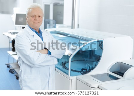 Proud scientist. Elderly scientist smiling posing proudly at his laboratory near modern analyzing machine copyspace research biology immunology medical industry profession experience health concept