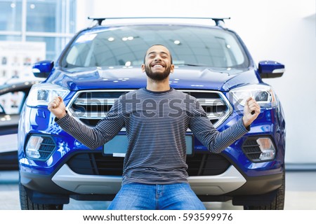 What a car! Happy handsome African man looking excited standing on his knees in front of his newly bought cool car expression emotions emotional winner victory winning arms raised victorious concept