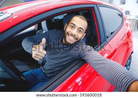 First car pic. Handsome young African man smiling making a selfie sitting in his new car at the dealership copyspace owner ownership driver mulatto buyer consumerism lifestyle travel concept