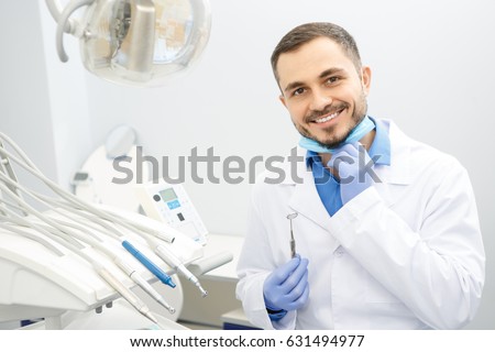 Professional male dentist smiling to the camera holding dental instruments sitting at his office copyspace dentistry profession doctor treatment curing help helpful skilled job worker health medical