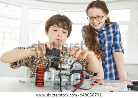 Young boy concentrating building a robot while his sister is smiling watching him standing near siblings kids children education learning lesson robotics school science hobby activity childhood family